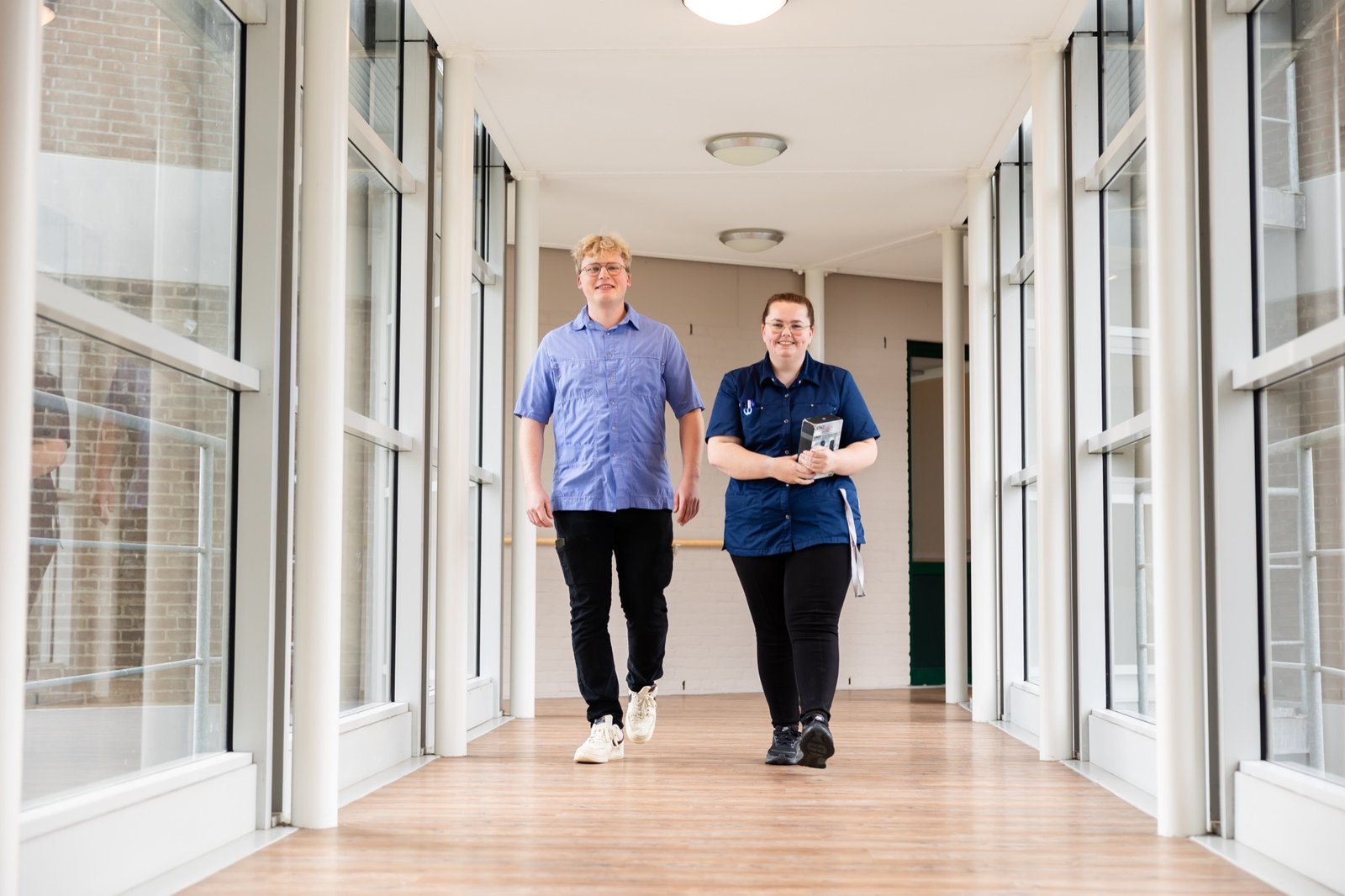 Twee medewerkers lopen samen door een lichte gang van De Koperhorst.
